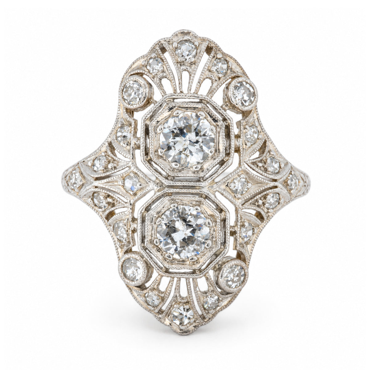 An antique Art Deco platinum cocktail ring featuring two central diamonds within an elaborate geometric filigree design, accented by smaller diamonds.