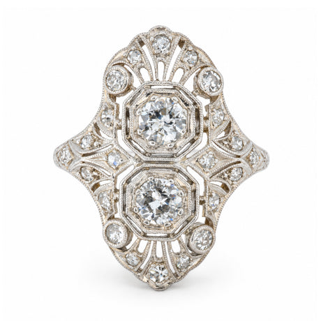 An antique Art Deco platinum cocktail ring featuring two central diamonds within an elaborate geometric filigree design, accented by smaller diamonds.