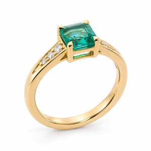 Vintage-inspired, Emerald and diamond flanked solitaire engagement ring shown from the side against white background