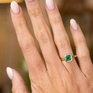 A close-up of a hand wearing an Antique-inspired, Emerald solitaire engagement ring in yellow gold.  