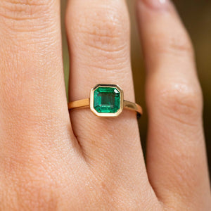 A close-up of a yellow gold Antique-inspired, Emerald solitaire engagement ring worn on a hand and showing off the detaiils of the stone. 