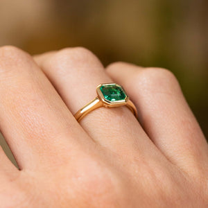 A close up Antique-inspired, Emerald solitaire engagement ring in yellow gold on a hand shown from the side to show profile on finger