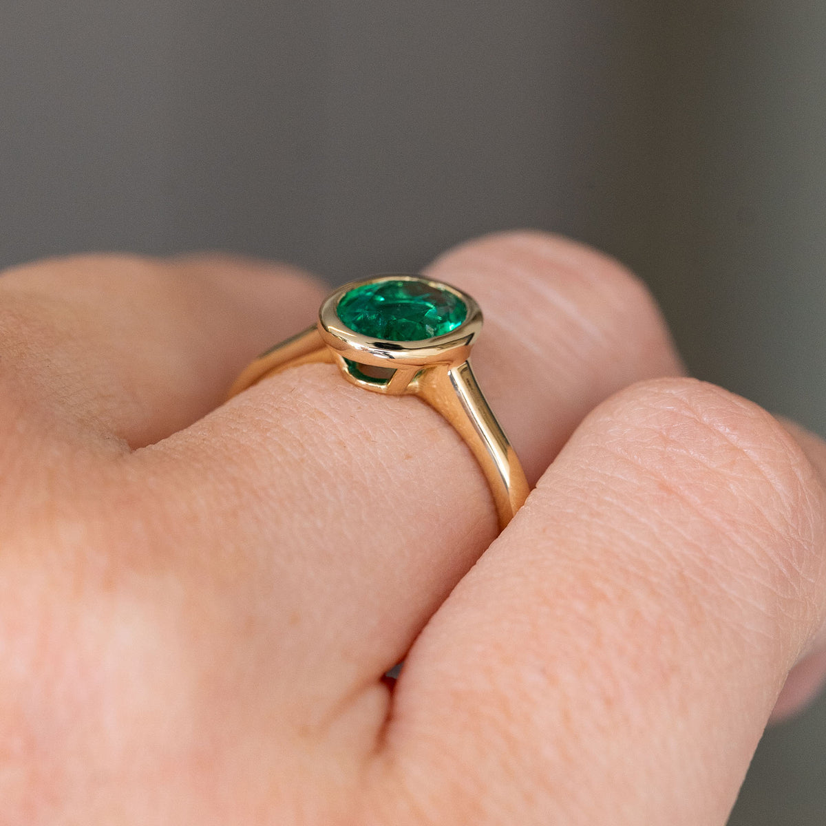 A close up of a Vintage inspired emerald solitaire engagement ring, showcasing the low profile of the ring when worn on the hand and the yellow gold rub-over setting and band. 