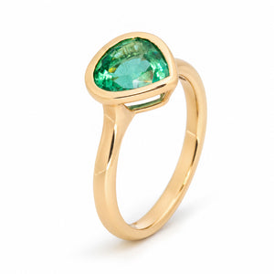 Elevated studio portrait of the emerald ring, revealing its pear-shaped centre stone, open gallery and polished gold band.