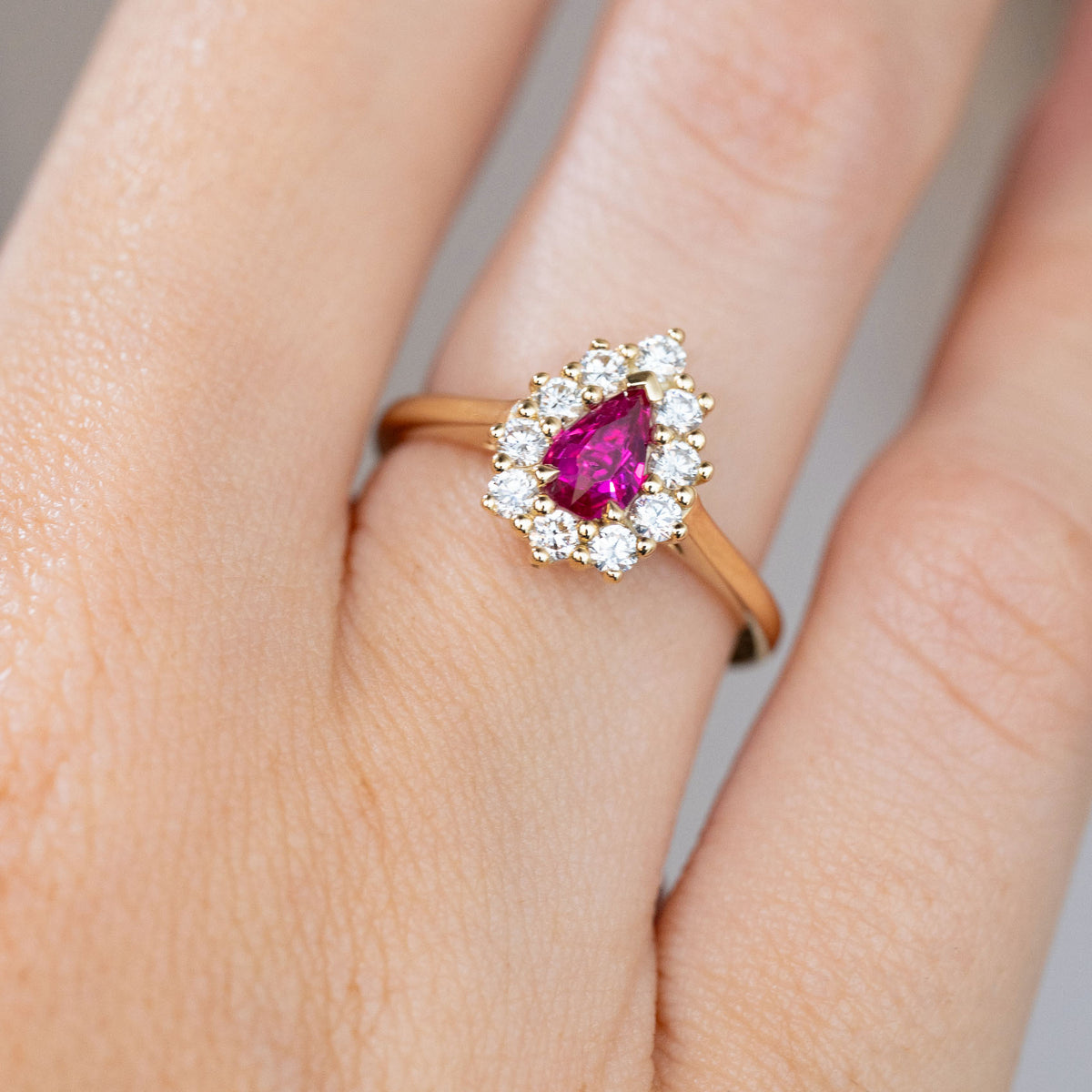 Close-up of the vintage-style engagement ring, with a rich pink-red pear-cut ruby encircled by brilliant diamonds.