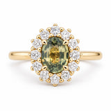 An antique-inspired yellow gold engagement ring with a green-yellow oval sapphire at the centre and a diamond halo.