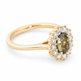 A vintage-inspired engagement ring with a green oval sapphire and diamond cluster in 14ct yellow gold.
