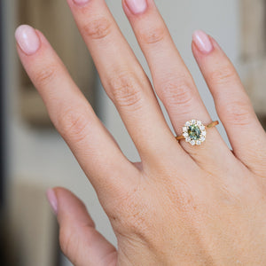 Worn on the hand, this yellow gold engagement ring displays the rich pine green sapphire and its classic oval diamond surround.