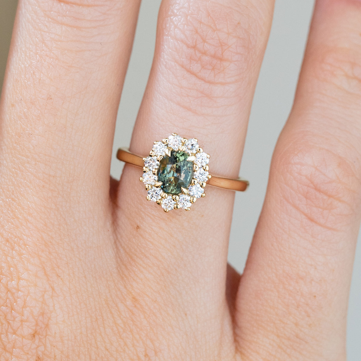 Closer worn view of an antique-style sapphire engagement ring, highlighting the deep green tones and individually set halo diamonds.