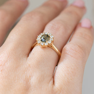 Oblique hand detail revealing the raised yellow gold setting, oval sapphire centre and sculptural round diamond cluster.