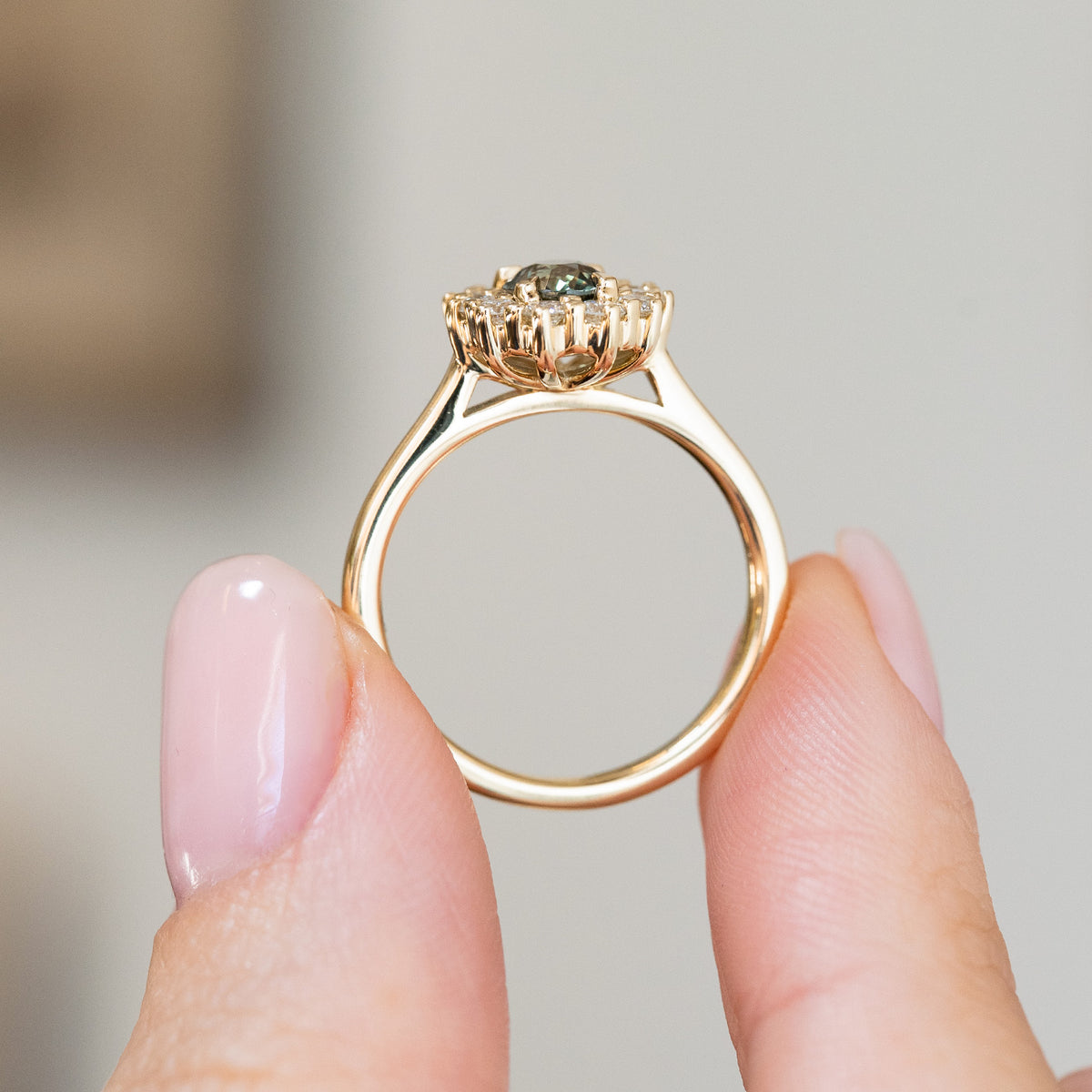 Reverse profile of the ring held between the fingers, displaying its open gallery, elevated cluster and slender yellow gold shank.