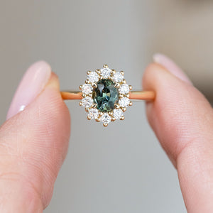 Held between the fingers, the engagement ring’s green sapphire centre and symmetrical round diamond cluster come into sharp focus.