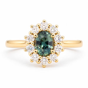 Oval green sapphire framed by a radiant cluster of round brilliant-cut diamonds in this antique-inspired yellow gold engagement ring.