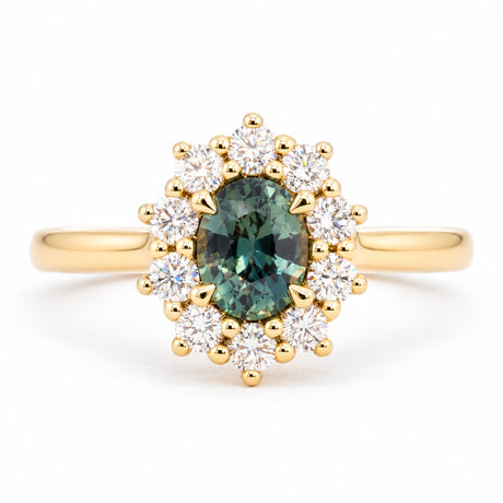 Oval green sapphire framed by a radiant cluster of round brilliant-cut diamonds in this antique-inspired yellow gold engagement ring.