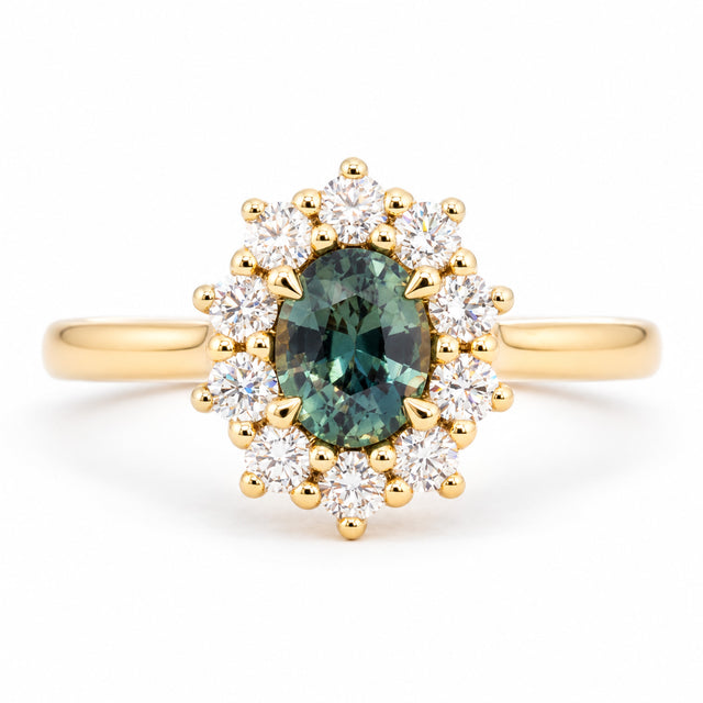 Oval green sapphire framed by a radiant cluster of round brilliant-cut diamonds in this antique-inspired yellow gold engagement ring.