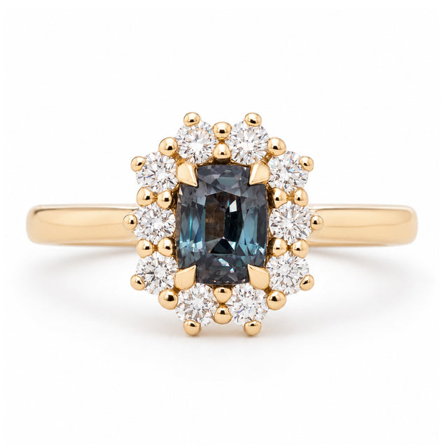 Antique-inspired blue sapphire and diamond cluster engagement ring in yellow gold, featuring a rectangular sapphire surrounded by brilliant-cut white diamonds.
