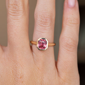 Close-up on-hand view of the faceted pink sapphire framed by a sleek geometric yellow gold surround.