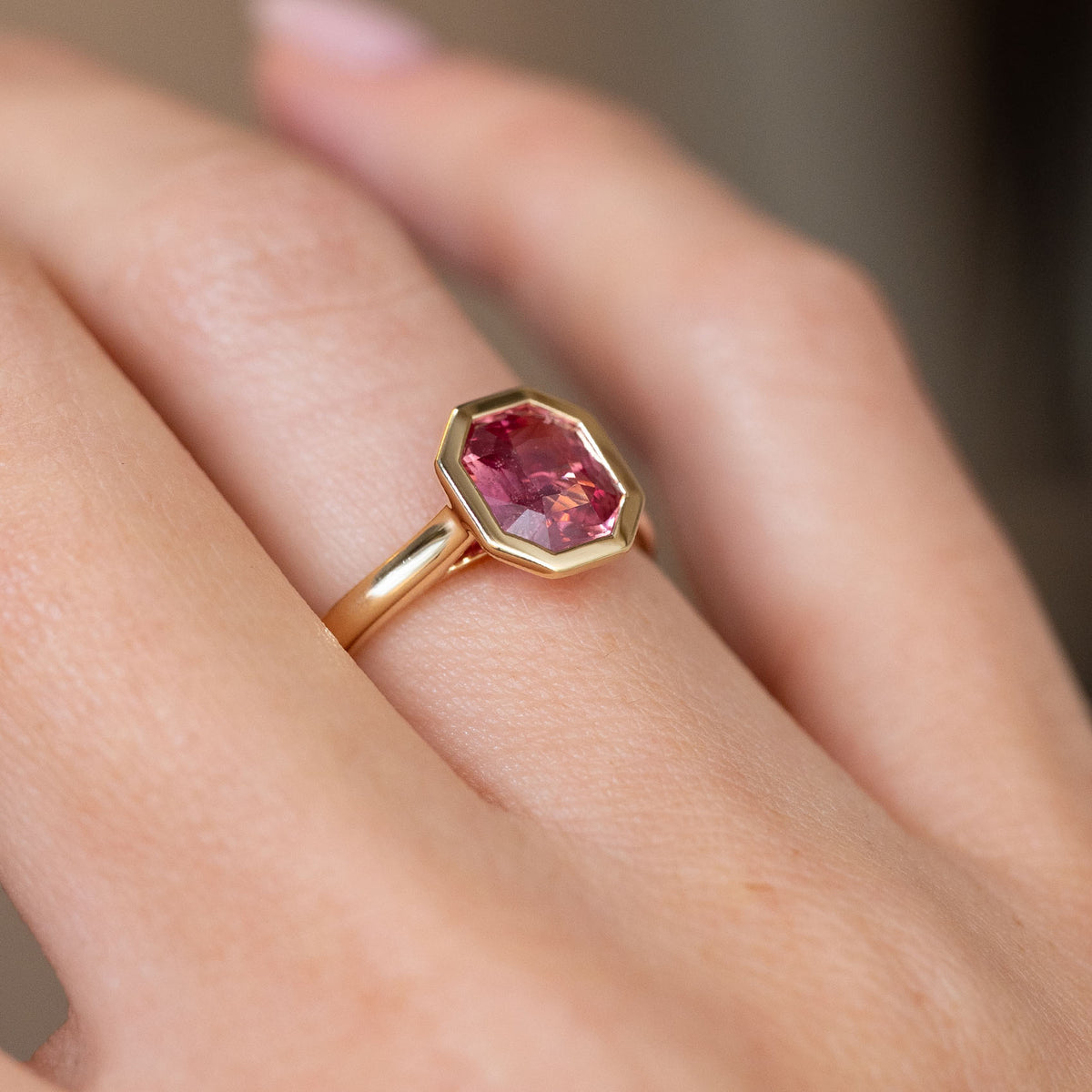 Three-quarter hand view revealing the raised peachy sapphire and slender polished gold shank.