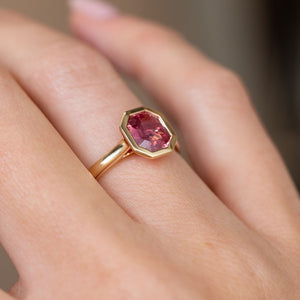 Three-quarter hand view revealing the raised peachy sapphire and slender polished gold shank.