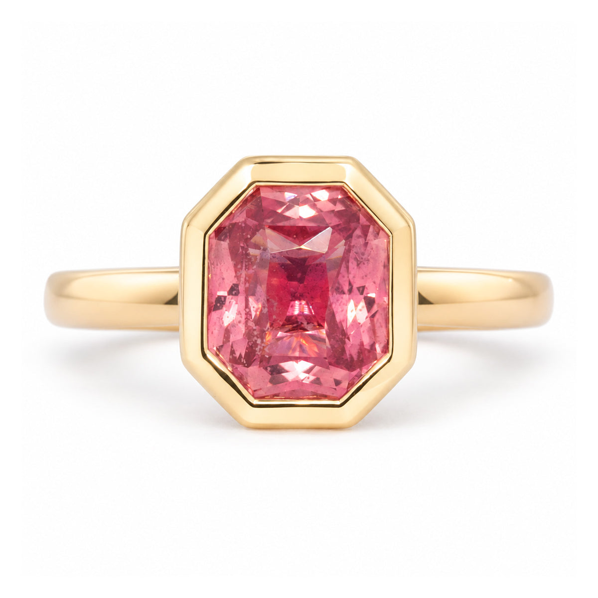 Antique-inspired peachy pink sapphire solitaire ring in yellow gold, featuring a rectangular faceted stone within an octagonal rub-over setting.