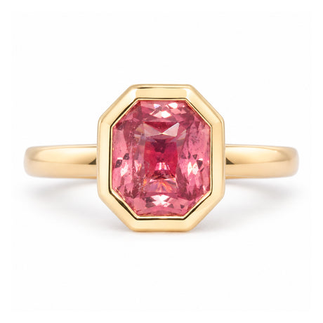 Antique-inspired peachy pink sapphire solitaire ring in yellow gold, featuring a rectangular faceted stone within an octagonal rub-over setting.