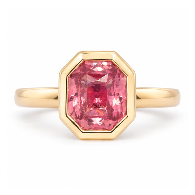 Antique-inspired peachy pink sapphire solitaire ring in yellow gold, featuring a rectangular faceted stone within an octagonal rub-over setting.