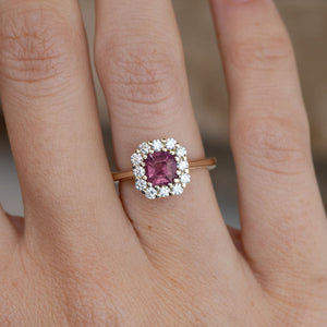 Close-up of the step-cut pink sapphire surrounded by brilliant-cut white diamonds, worn on a finger.