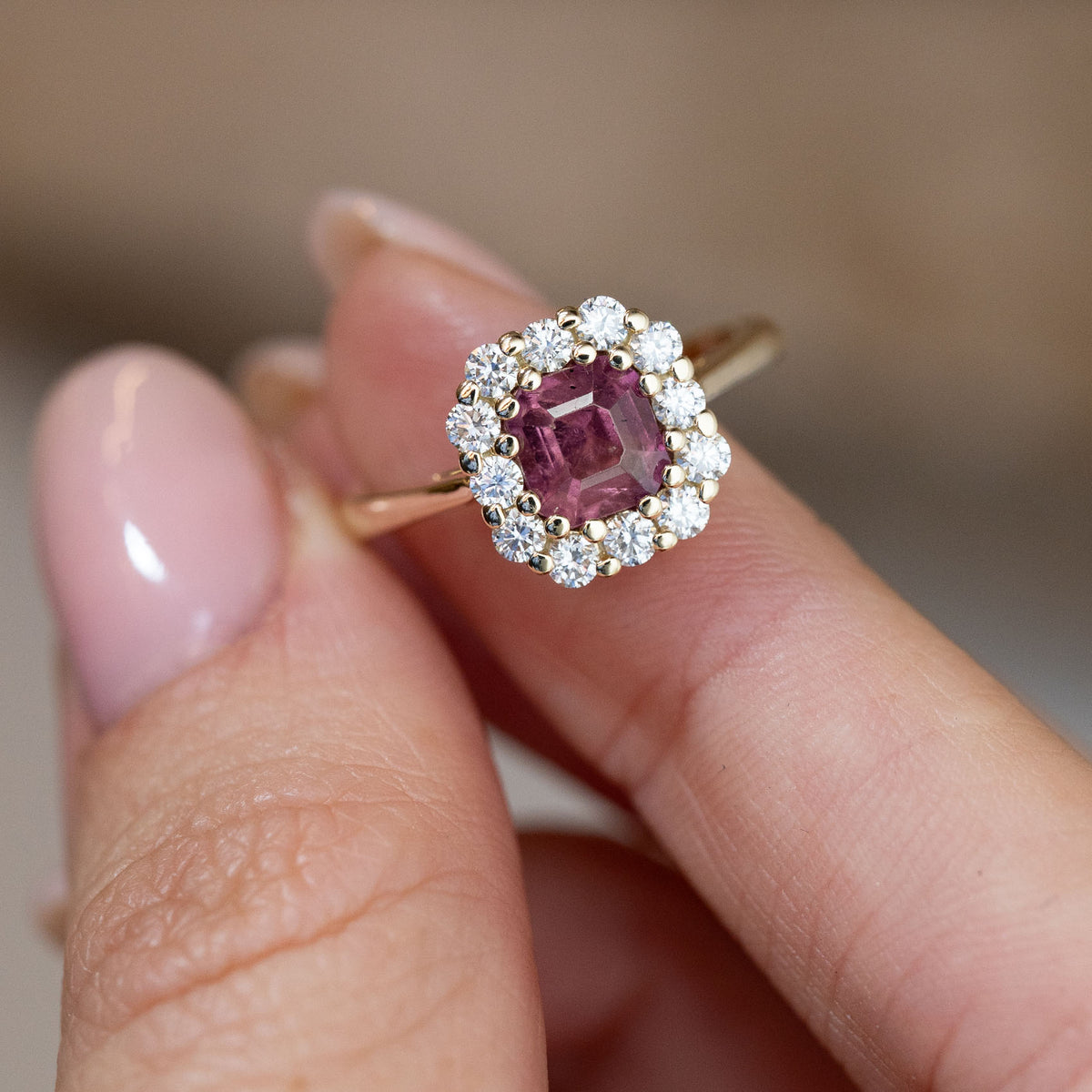 Hand-held close-up of the rectangular step-cut pink sapphire framed by sparkling white diamonds in yellow gold.