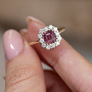 Hand-held close-up of the rectangular step-cut pink sapphire framed by sparkling white diamonds in yellow gold.