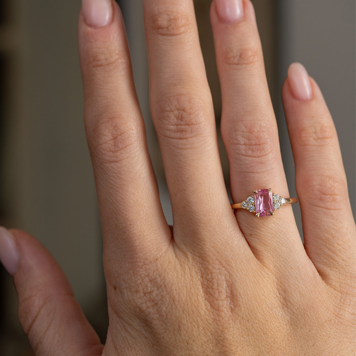 Vintage-inspired pink sapphire engagement ring worn on the hand, showing the elegant scale of its diamond-accented yellow gold design.