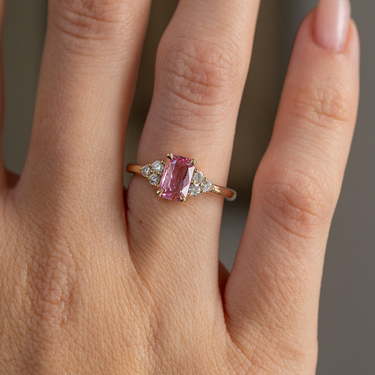 Close hand detail highlighting the soft pink sapphire, three-diamond shoulder clusters and polished yellow gold band.