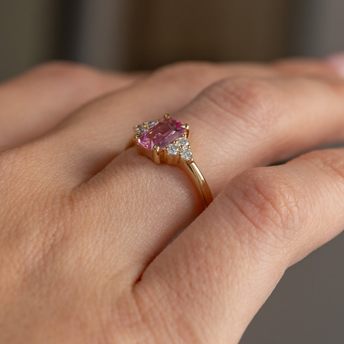 Three-quarter view of the ring being worn, revealing the raised pink sapphire setting and sculpted diamond shoulders.
