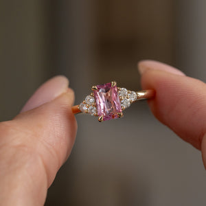 Handheld close-up of the rectangular pink sapphire framed by sparkling trefoil diamond clusters in yellow gold.