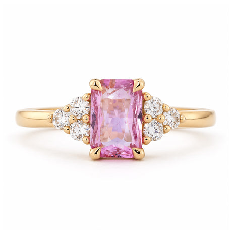 Vintage-inspired pink sapphire and diamond trefoil engagement ring in yellow gold, with a rectangular centre stone and clustered diamond shoulders.