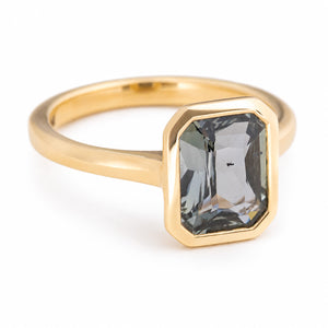 An Antique-inspired, Charcoal-teal sapphire solitaire engagement ring in yellow gold against a white background, set on a angle to show the side profile of the ring.