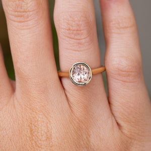 A close-up of a hand wearing a Vintage-inspired yellow gold solitaire ring with a round pale pink sapphire in a bezel setting.