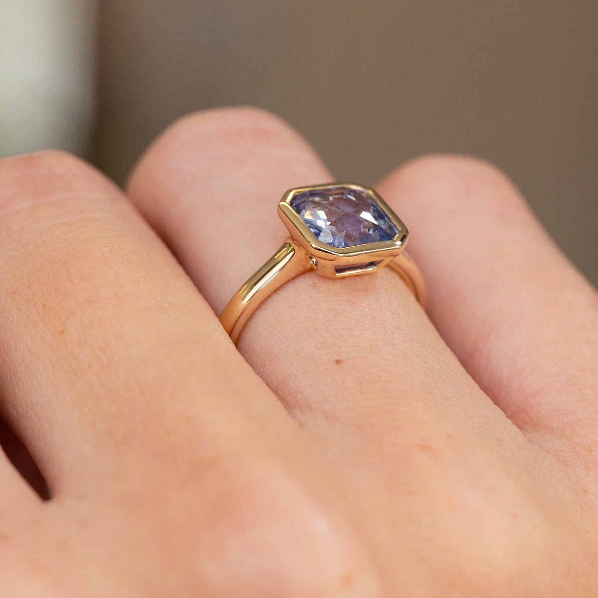 Three-quarter view revealing the raised rub-over setting and open gallery beneath the sapphire.