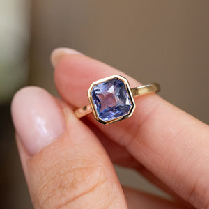 Lavender sapphire solitaire held between the fingers, offering a detailed look at its facets and cut corners.