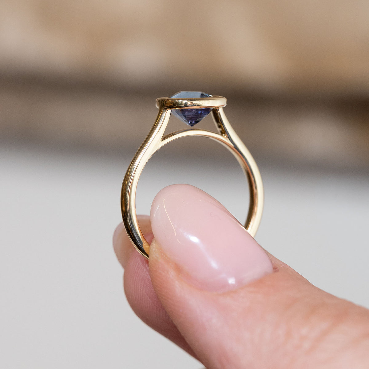 Side profile of the sapphire solitaire engagement ring, revealing the elevated open gallery and delicate yellow gold band.