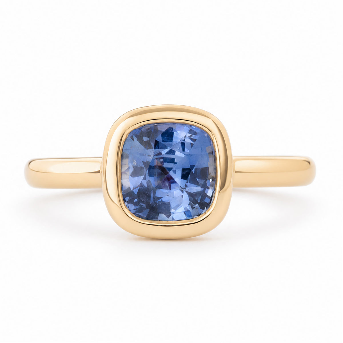 Antique-inspired blue cushion-cut sapphire solitaire engagement ring in yellow gold, featuring a polished bezel setting and elegant gold band.