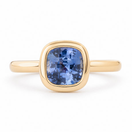 Antique-inspired blue cushion-cut sapphire solitaire engagement ring in yellow gold, featuring a polished bezel setting and elegant gold band.