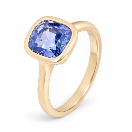 An angled photograph of the sapphire solitaire ring, showcasing its purple-blue hues and polished yellow gold band.