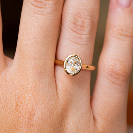 A close-up of a hand wearing a yellow gold vintage inspired solitaire engagement ring with a bezel-set round yellow sapphire. 