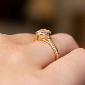 A close up of the side profile of an Antique-inspired, pale yellow sapphire solitaire engagement ring worn on a finger.  Showcasing the yellow gold setting and band which allows a wedding band to sit closely alongside the ring once worn. 
