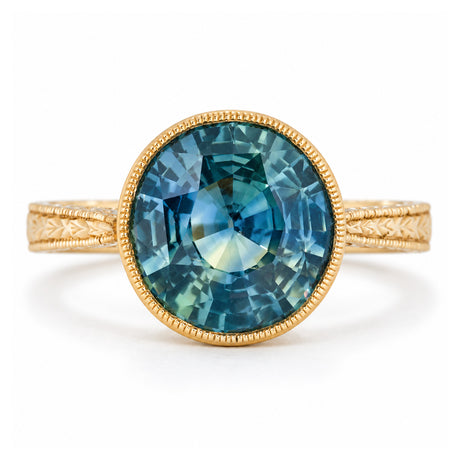 Antique-inspired Montana blue-green sapphire solitaire ring in yellow gold, featuring a round gemstone with a milgrain bezel and engraved band.