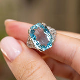 Antique Art Deco aquamarine cocktail ring held between the fingers, showcasing the gemstone’s pale blue facets and geometric diamond detailing.