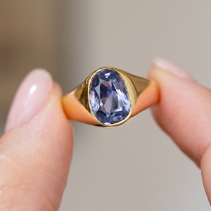 Ceylon blue-violet sapphire ring held between the fingers, displaying the gemstone and polished yellow gold shoulders.