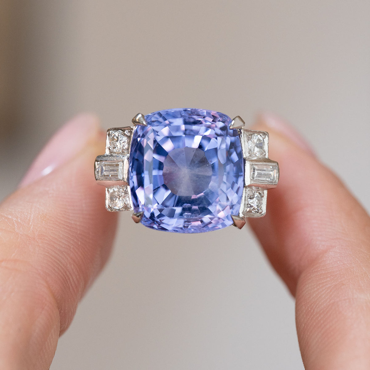 Violet-blue sapphire cocktail ring held between the fingers, showing the diamond accents and impressive centre stone.
