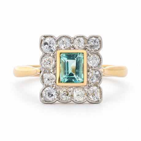 Front view of an antique Edwardian engagement ring featuring a mint green step-cut emerald and old-mine cut diamond cluster in yellow gold and platinum.
