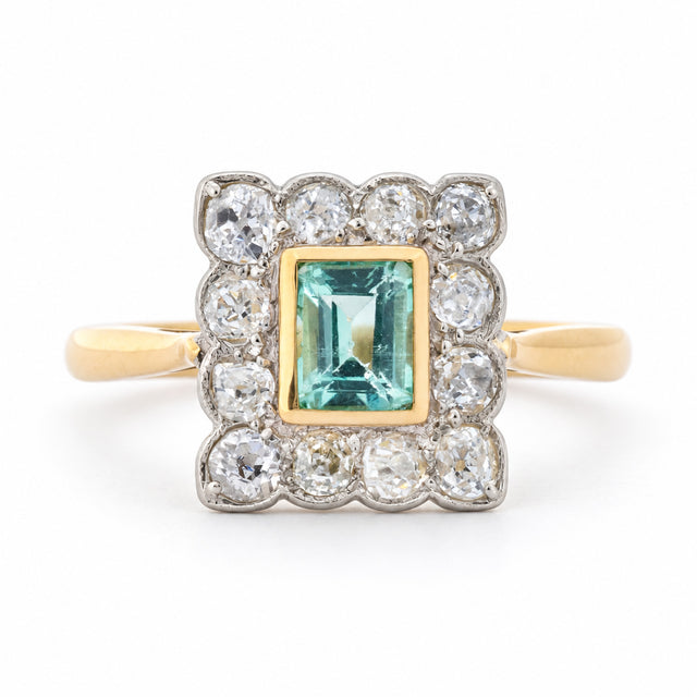 Front view of an antique Edwardian engagement ring featuring a mint green step-cut emerald and old-mine cut diamond cluster in yellow gold and platinum.